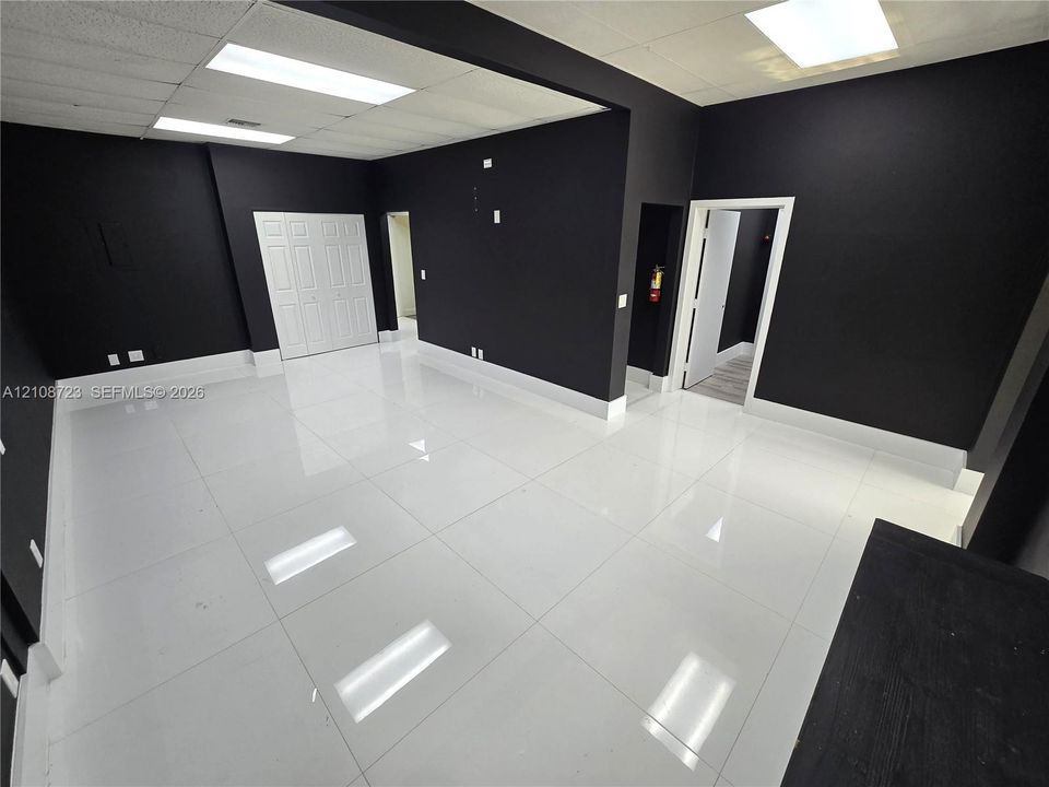 High-gloss white tile flooring, bold matte black wall finishes, inset drop-ceiling lighting, and white six-panel closet doors
