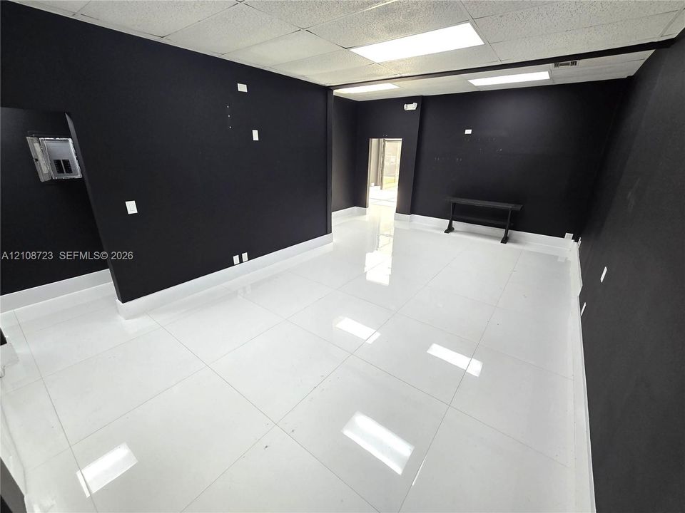 Interior space featuring high-gloss, large-format white tile flooring, contrasting matte black wall finishes, and integrated recessed panel lighting