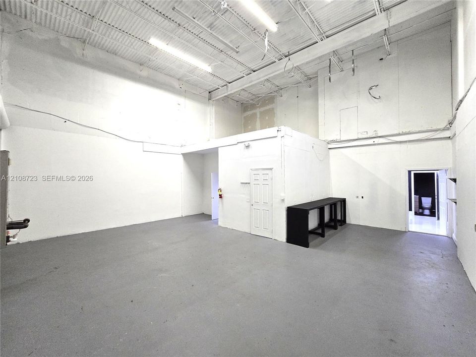 Expansive interior featuring high ceilings with exposed metal trusses, painted masonry walls, durable industrial-style flooring, and built-in counter cabinetry
