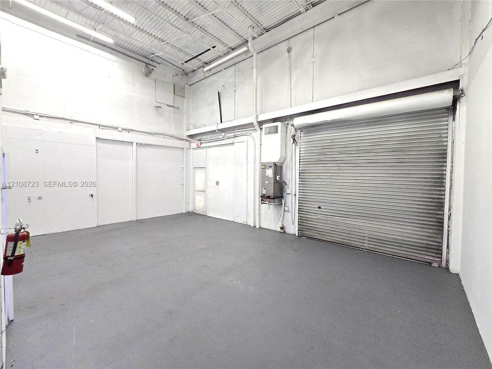 Open-concept industrial workspace featuring high ceilings, exposed corrugated metal roof decking, a roll-up bay door, and durable epoxy-coated flooring