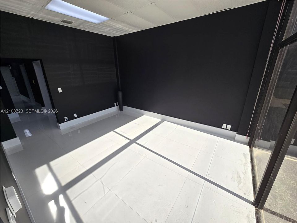Interior space featuring high-contrast matte black wall finishes, large-format white tile flooring, suspended drop ceiling with recessed lighting, and expansive floor-to-ceiling glass paneling
