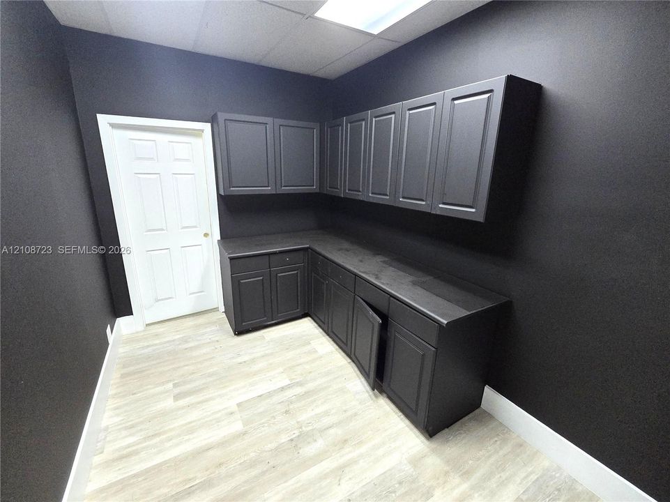 L-shaped cabinetry featuring matte-finish charcoal surfaces, integrated upper and lower storage, wood-finish flooring, and a six-panel interior door
