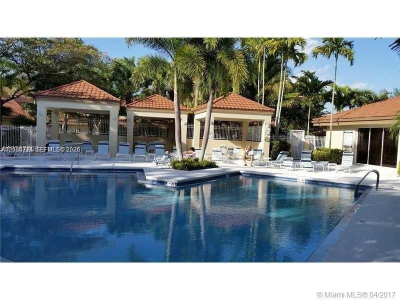 In-ground swimming pool featuring a tiled perimeter and concrete decking, surrounded by multiple covered pavilion structures with clay-tile roofs and mature palm trees