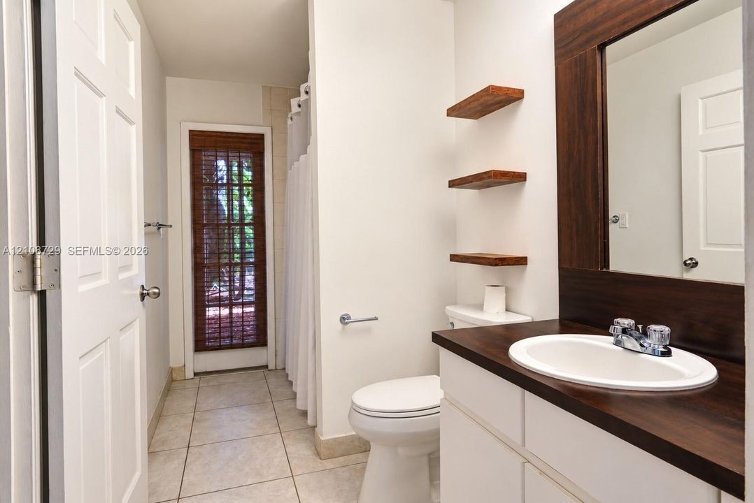Bathroom featuring a door with access to the pool, white vanity with a dark wood-finish countertop, integrated oval sink, floating wood shelving, and tile flooring