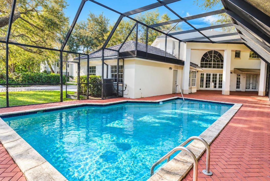 Screened-in outdoor area featuring a swimming pool, red brick paver decking, and an arched transom window