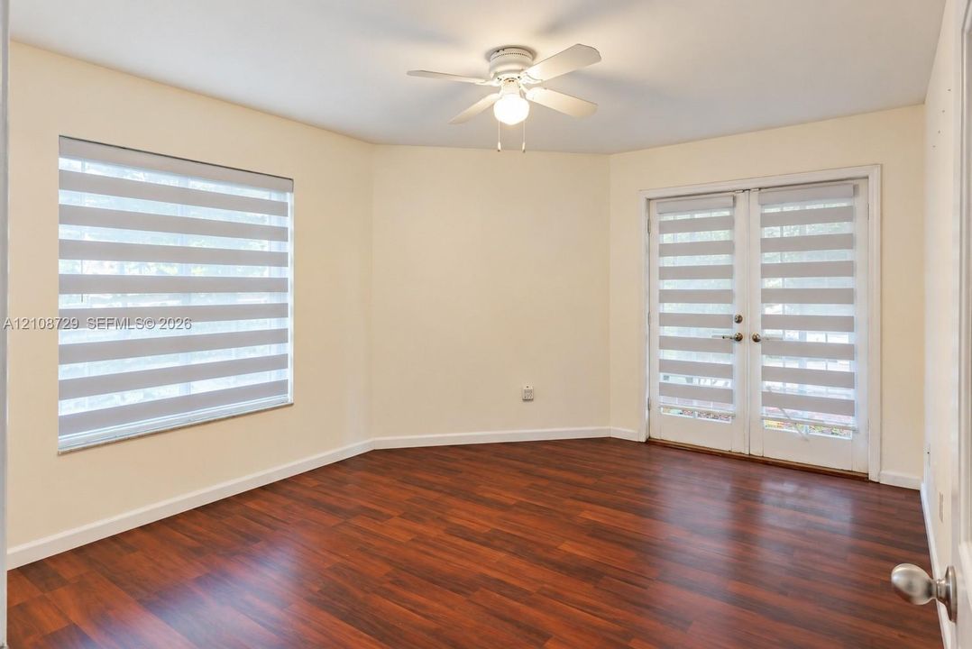 Downstairs bedroom Wood-laminated flooring, multi-pane window zebra-style shades displayed for photography only. Ceiling fan with light fixture, and double glass-panel doors