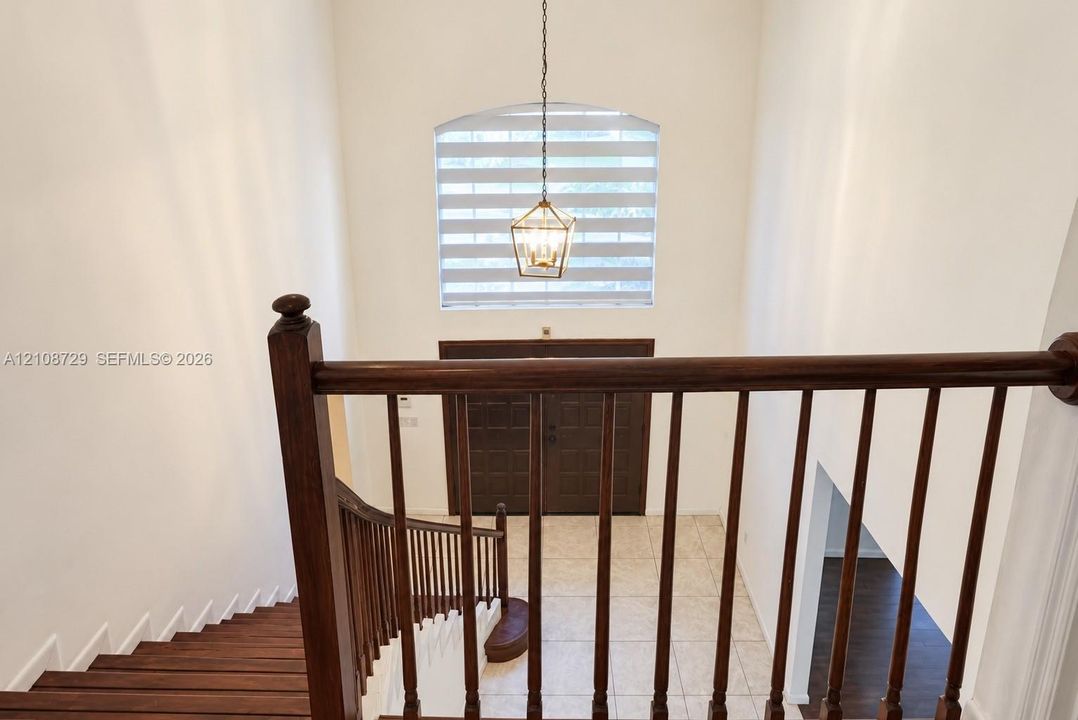Double-height entryway featuring a wood-finish staircase with a turned-wood railing, arched window, metal-frame pendant lighting, and a set of paneled double front doors
