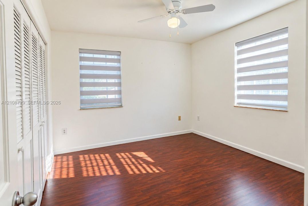 Bedroom upstairs featuring wood-laminated flooring, dual windows with ceiling fan with integrated lighting, and louvered closet doors. zebra-style shades displayed for photography only.