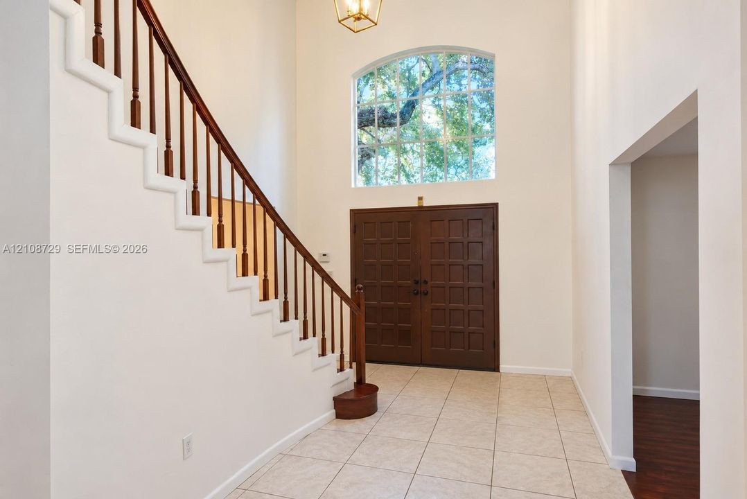 Double-height foyer featuring ceramic tile flooring, a staircase with wood railings, a large arched window, and double entry doors