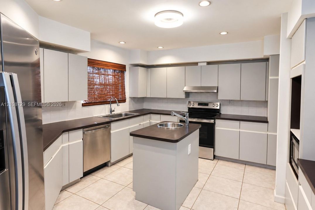 Kitchen featuring flat-panel cabinetry, a central island with a circular basin, stainless steel appliances, dark composite countertops, and tile flooring