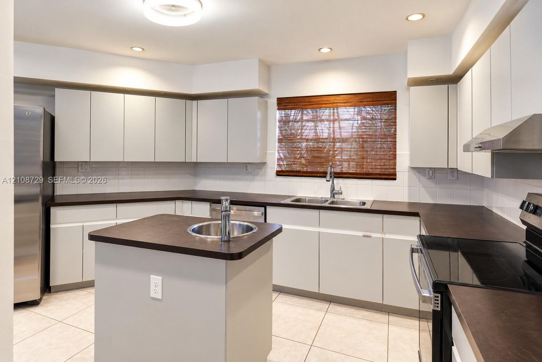 Kitchen featuring matte cabinetry, dark countertops, a center island with a secondary sink, stainless steel appliances, and tile flooring