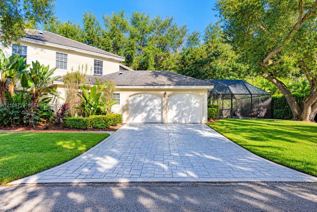 Two-story exterior featuring a stone-paver driveway, a two-car garage with arched entries, and a screened-in lanai