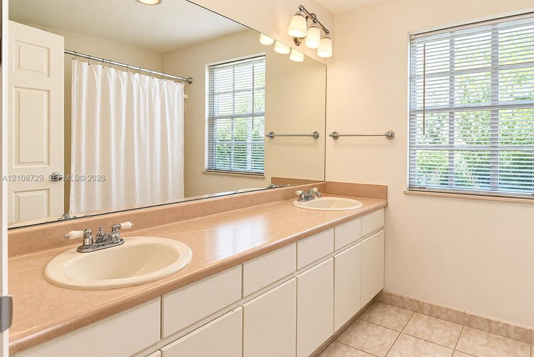 Bathroom upstairs. Dual-sink vanity upstairs with solid-surface countertop, full-width wall mirror, tiled flooring, and chrome hardware fixtures
