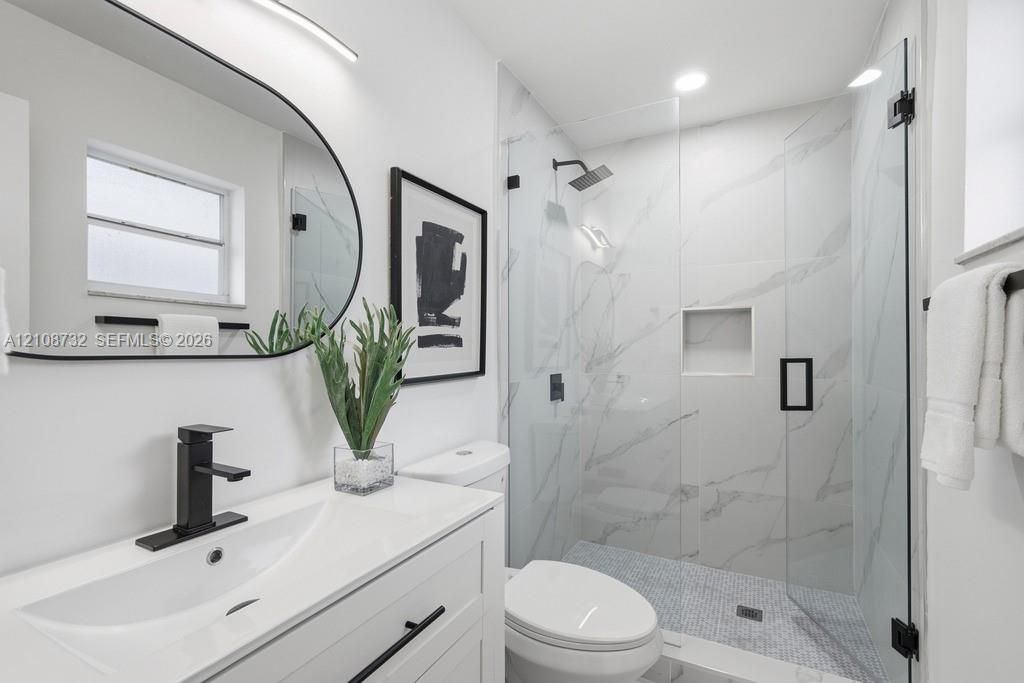 Modern vanity with a rectangular sink, matte black faucet, and curved mirror, complemented by a walk-in shower featuring large-format stone-look wall tiles, a built-in recessed niche, and a glass enclosure with matte black hardware