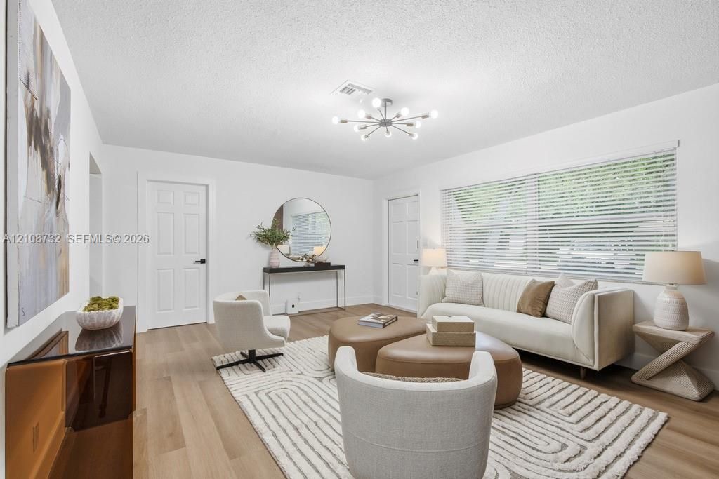Living area featuring wood-finish flooring, a modern multi-arm sputnik chandelier, and a large window with horizontal blinds