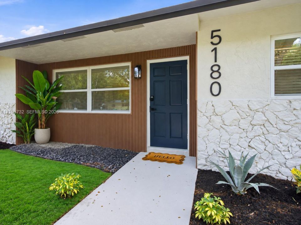 Exterior entry featuring a dark blue six-panel door, vertical wood-slat siding, white textured stone facade, and a concrete walkway