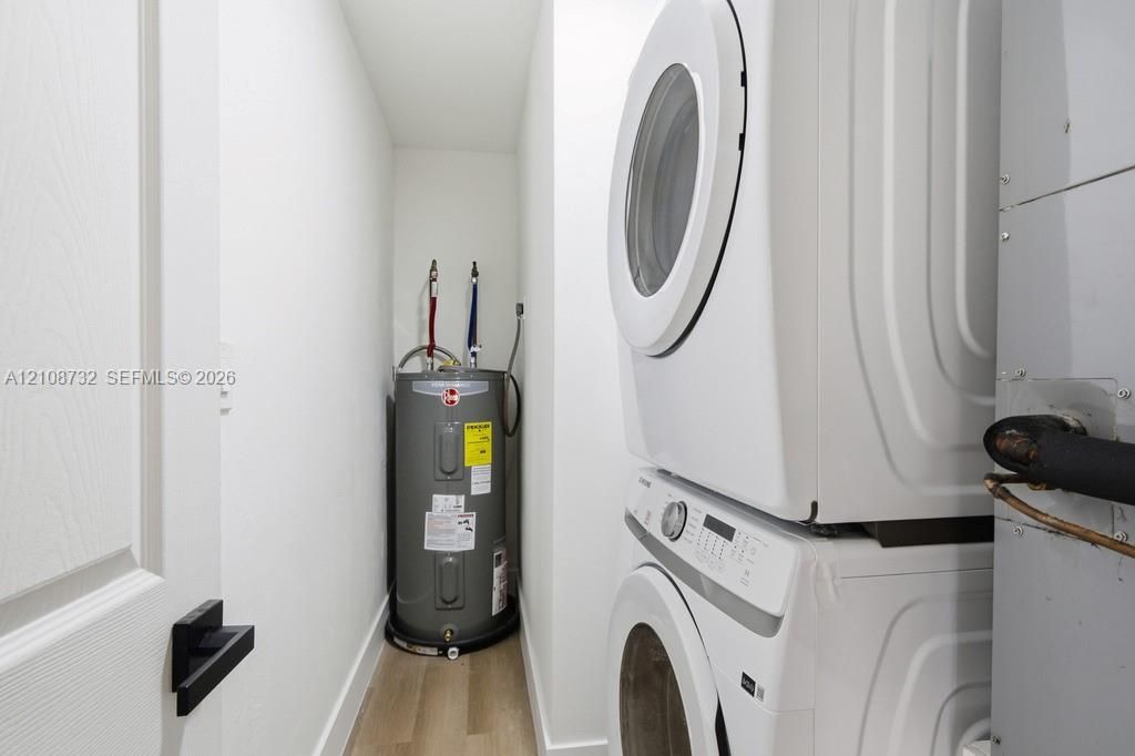 Utility closet featuring stackable laundry appliances, a water heater, and wood-finish flooring