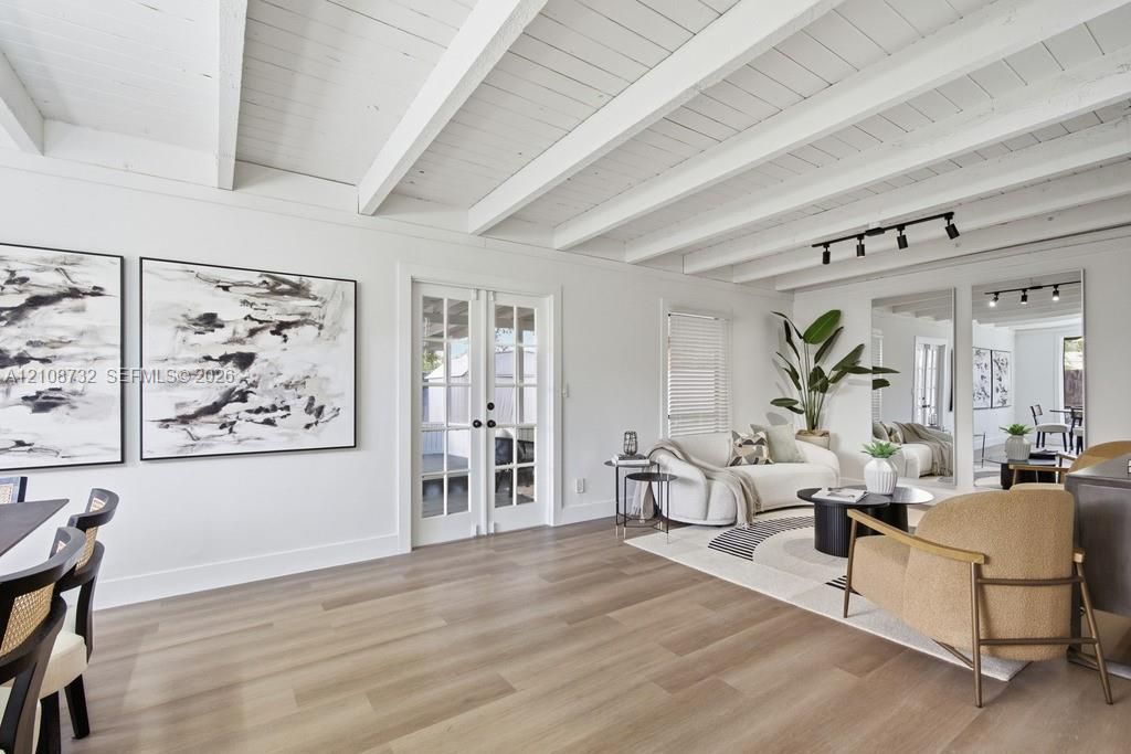 Vaulted ceilings featuring exposed white-painted beams, light wood-finish flooring, glass-paned French doors, and ceiling-mounted track lighting