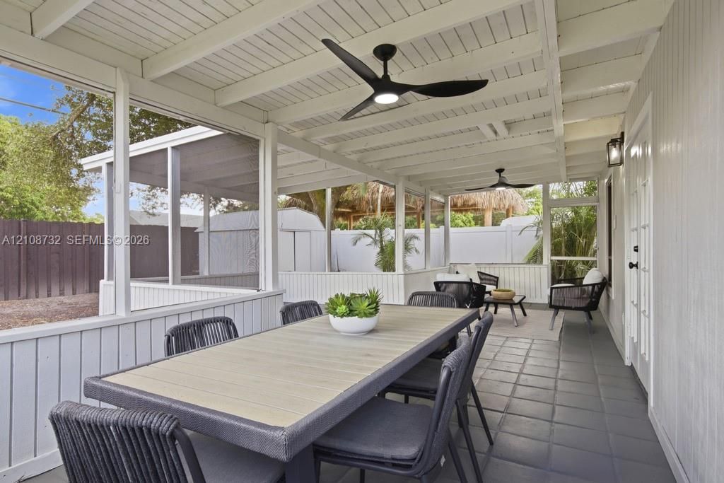 Screened-in porch featuring a painted wood-beamed ceiling, integrated ceiling fans, tiled flooring, and white paneled walls