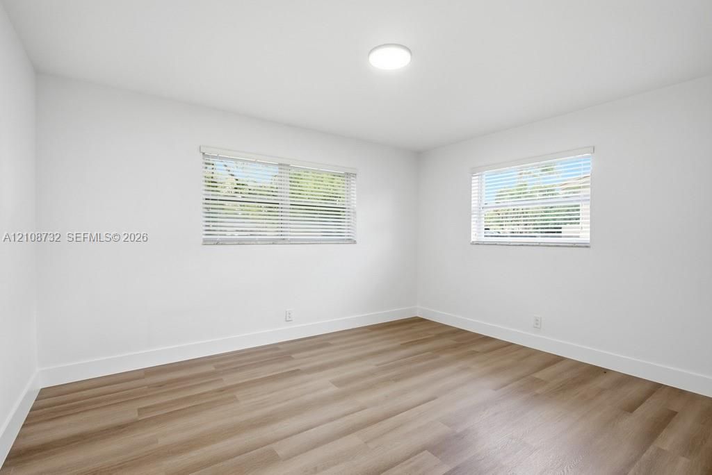 Interior room featuring wood-finish flooring, two dual-pane windows with horizontal blinds, and a circular flush-mount ceiling light