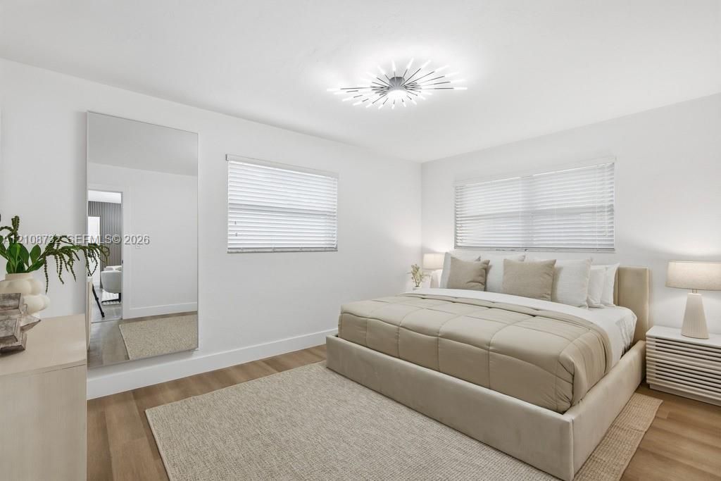 Neutral-toned interior featuring wood-finish flooring, full-length wall mirror, horizontal window blinds, and a contemporary sunburst-style flush mount ceiling light fixture