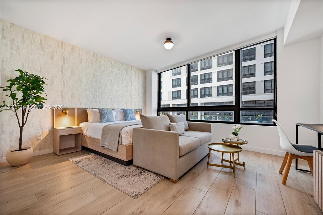 Room featuring floor-to-ceiling windows, wood-finish flooring, a textured accent wall, and integrated bedside shelving with wall-mounted lighting