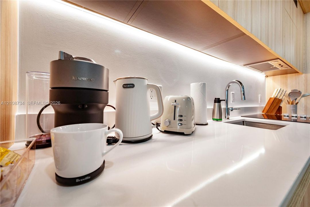 Solid surface countertop, under-cabinet LED task lighting, custom flat-panel cabinetry, and integrated stainless steel undermount sink with high-arc faucet