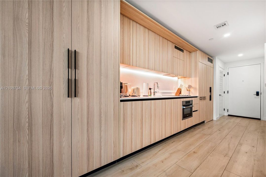 Floor-to-ceiling light wood-finish cabinetry, integrated wall oven, sleek under-cabinet task lighting, and wood-finish flooring