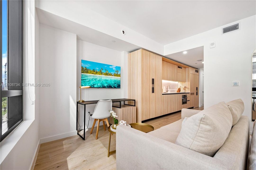 Kitchen area featuring wood-finish cabinetry, under-cabinet lighting, and built-in appliances, accented by wood-finish flooring and floor-to-ceiling windows