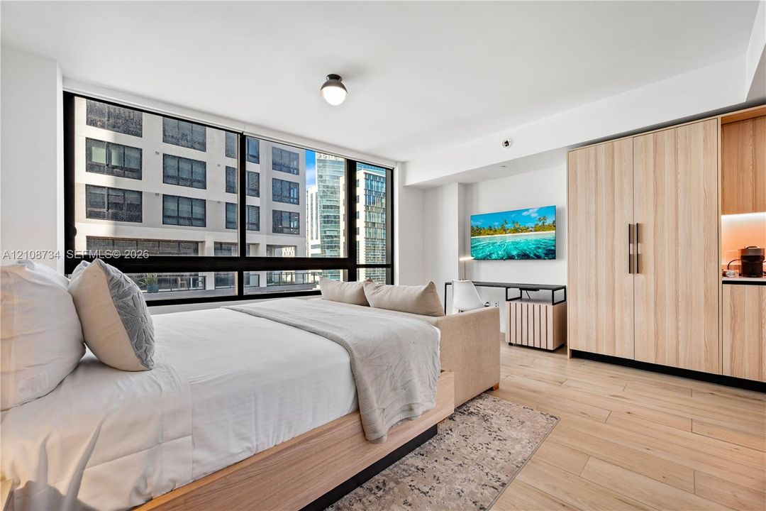 Floor-to-ceiling windows with dark framing, wood-finish flooring, and light wood-tone cabinetry