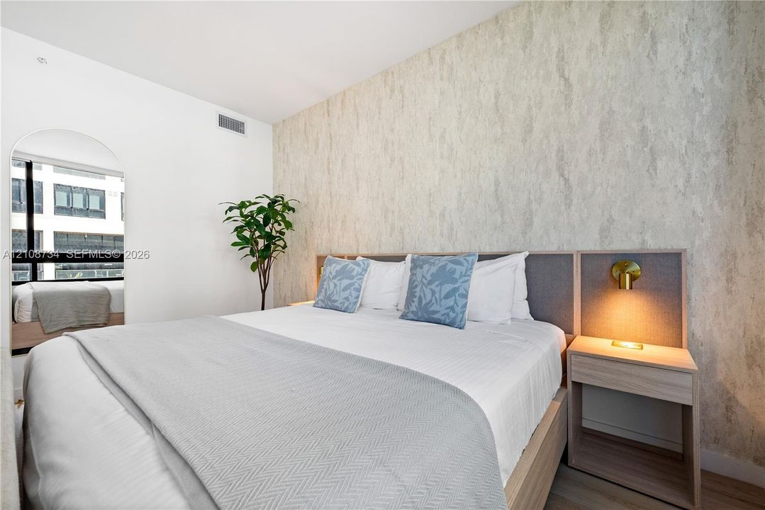 Textured wallpaper accent wall, built-in wooden nightstand with attached wall-mounted lighting, and arched mirror