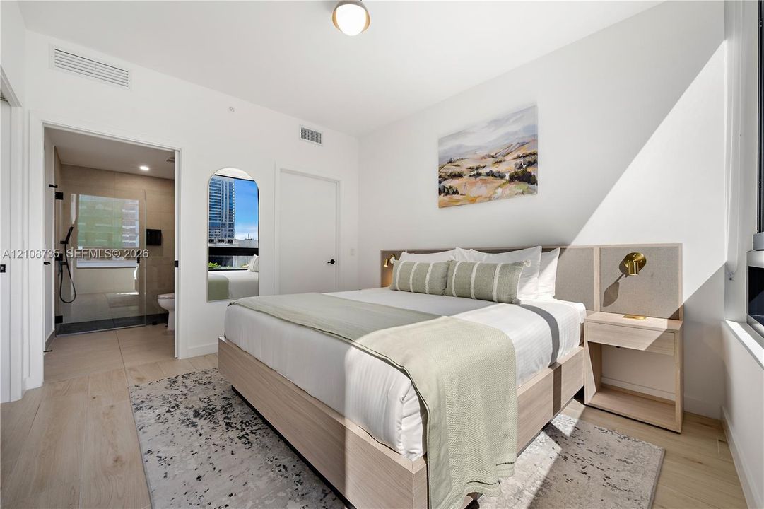 Bedroom featuring light wood-finish flooring, a built-in headboard with integrated lighting, and an arched wall mirror