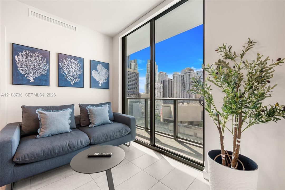 Floor-to-ceiling sliding glass doors, private balcony with metal railing, light-colored tile flooring, and urban skyline backdrop