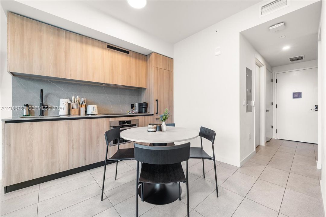 Kitchen featuring wood-finish flat-panel cabinetry, full-height tile backsplash, integrated stainless steel appliances, and large-format tile flooring