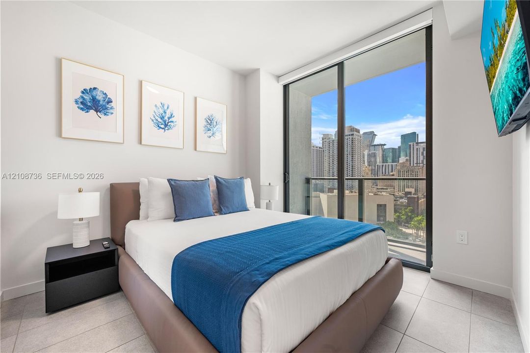 Floor-to-ceiling glass sliding doors, private balcony, neutral large-format tile flooring, and urban cityscape backdrop
