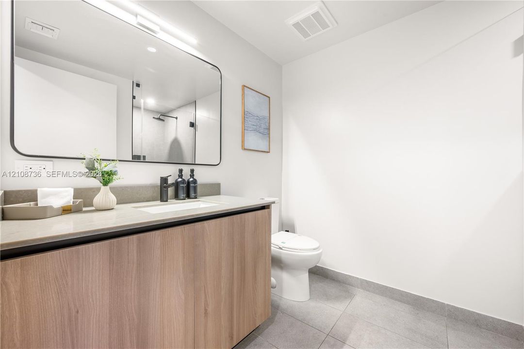 Floating wood-finish vanity with a stone countertop, integrated sink, matte black faucet, and large rectangular mirror with integrated lighting