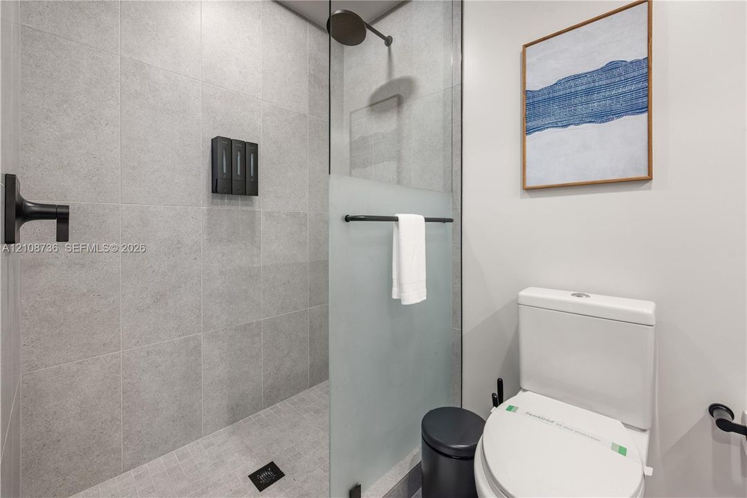 Walk-in shower featuring large-format grey tile, a glass partition with a frosted privacy panel, and matte black fixtures including a wall-mounted shower head and faucet