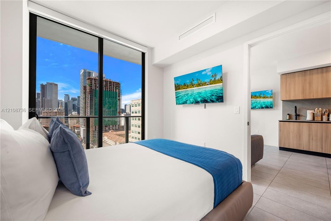 Floor-to-ceiling windows, city skyline backdrop, wood-finish cabinetry, tile flooring, and neutral wall finishes