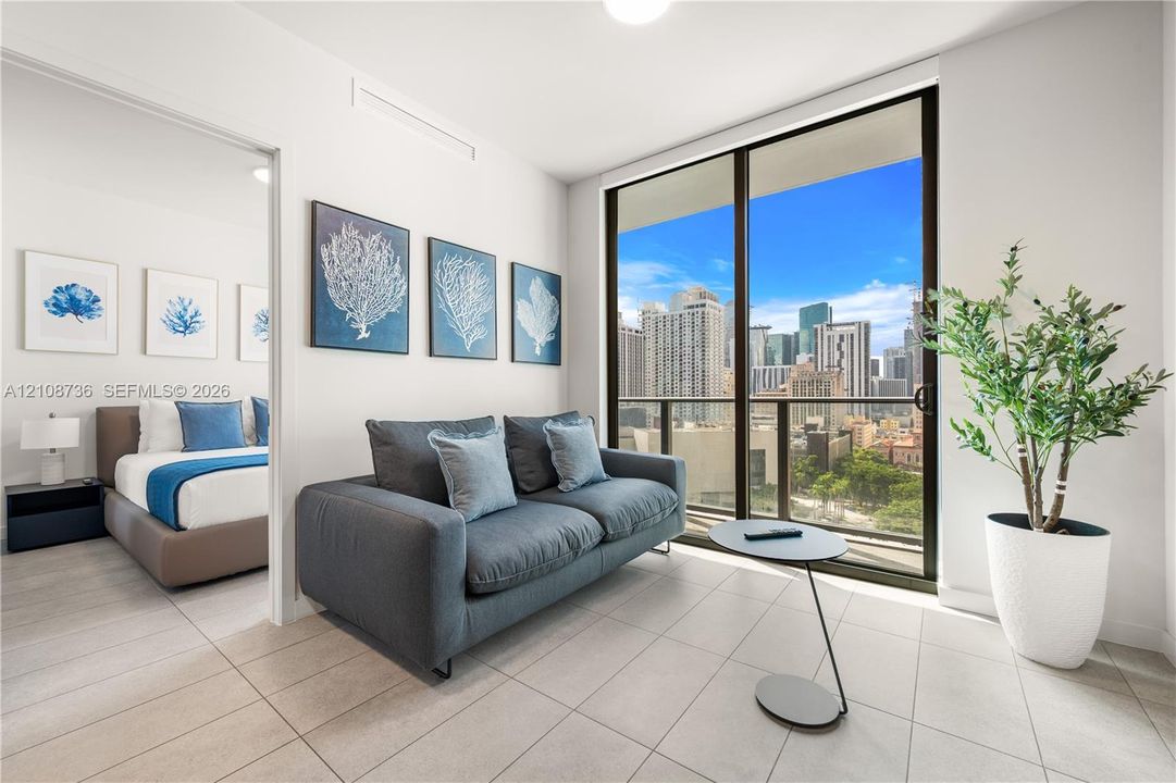 Floor-to-ceiling sliding glass doors, neutral tile flooring, and a private balcony featuring urban scenery