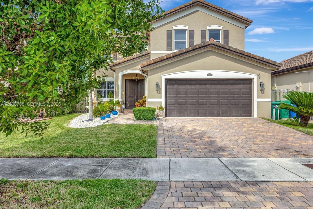 Two-story residence featuring a stucco facade, a multi-paneled garage door, a paved driveway, a tiled roof, and exterior shutter accents