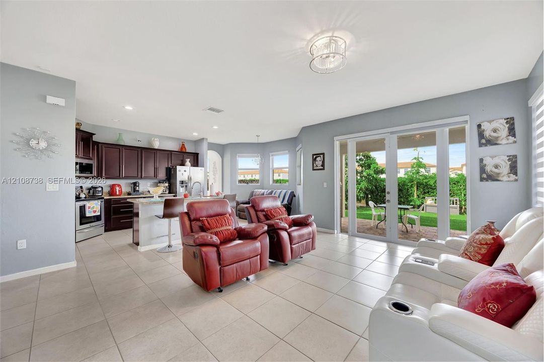 Open-concept kitchen featuring dark wood cabinetry, a stone-surfaced kitchen island, tile flooring, and glass-paneled sliding doors to the exterior