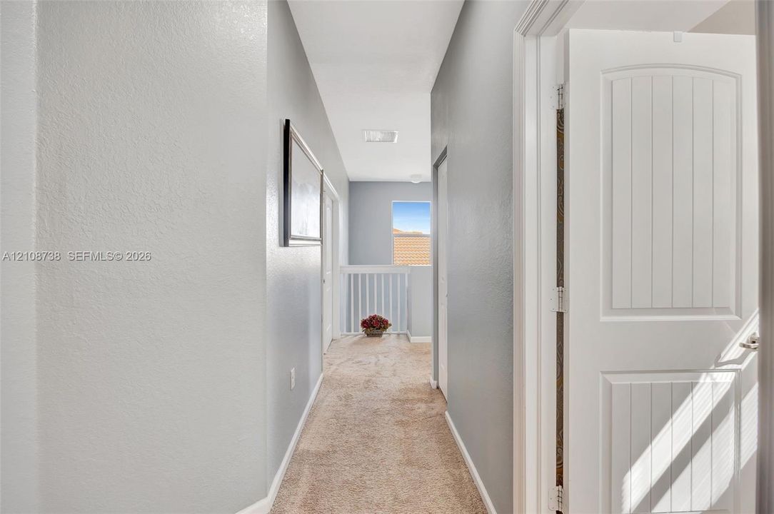 Hallway featuring neutral-toned carpeting, two-panel interior doors, light-colored wall paint, and a decorative railing