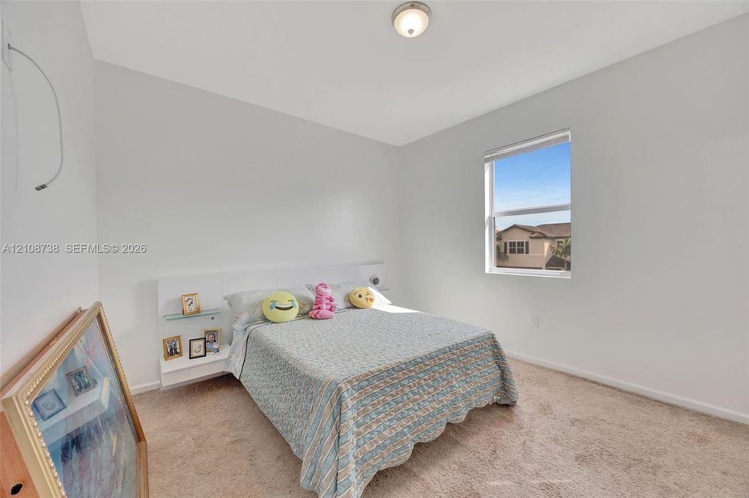 Neutral-toned walls, high ceilings, carpeted flooring, built-in headboard with integrated shelving, and a single-pane window