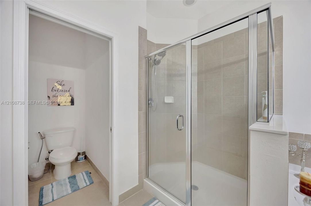 Walk-in shower featuring a glass enclosure, neutral tile surround, and adjustable handheld showerhead, accompanied by a separate water closet area
