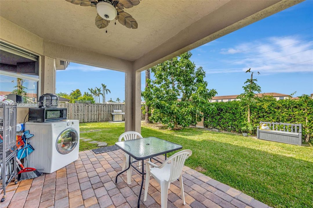 Covered patio featuring paver flooring and a ceiling fan, opening to a fenced backyard with a manicured lawn and mature landscaping