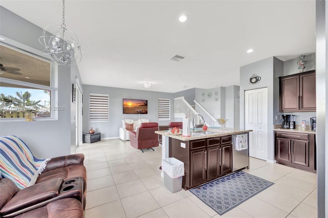 Open-concept interior featuring large-format tile flooring, a kitchen island with stone surfacing, espresso-toned cabinetry, recessed lighting, and a modern sculptural pendant fixture