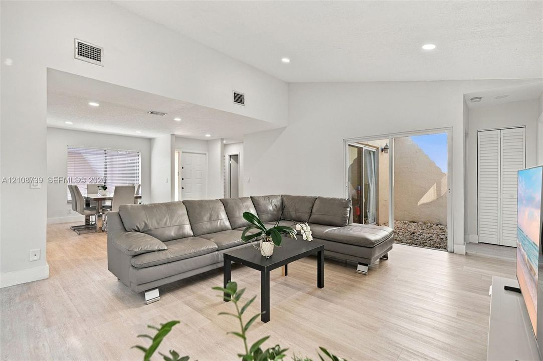 Vaulted ceilings, light-tone wood-finish flooring, recessed lighting, and a sliding glass door providing external access