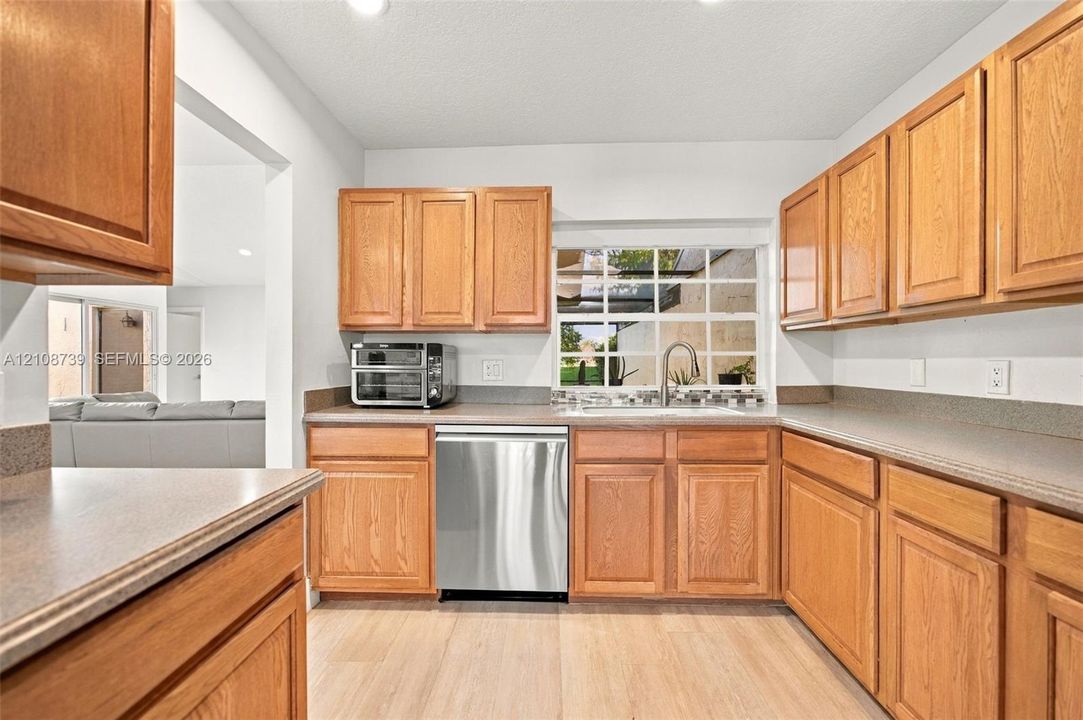 Kitchen featuring wood cabinetry, stainless steel dishwasher, solid-surface countertops, and wood-finish flooring