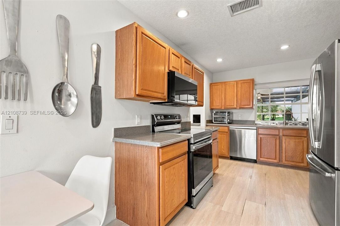 Kitchen featuring light wood-finish cabinetry, solid-surface countertops, recessed lighting, and stainless steel appliances