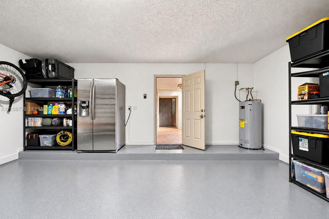 Garage interior featuring a finished grey epoxy floor, stippled ceiling, and a dedicated utility area